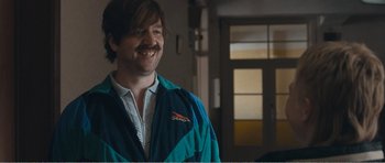 Movie still from “The Misfortunates” (2009), directed by Felix van Groeningen – A man in a blue and white jacket smiling; Medium shot, Over the shoulder angle