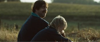 Movie still from “The Misfortunates” (2009), directed by Felix van Groeningen – A man and a boy riding a bike in a field; Close Up shot, Over the shoulder angle