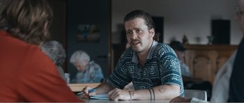 Movie still from “The Misfortunates” (2009), directed by Felix van Groeningen – A man sitting at a table writing on a piece of paper; Medium shot, Over the shoulder angle