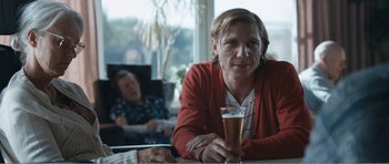 Movie still from “The Misfortunates” (2009), directed by Felix van Groeningen – A woman sitting at a table holding a glass of beer; Medium shot, Over the shoulder angle