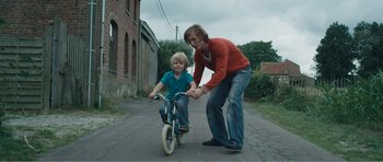 Movie still from “The Misfortunates” (2009), directed by Felix van Groeningen – A woman helping a boy ride a bike; Medium shot, Low angle