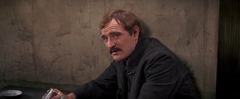 Movie still from “The Molly Maguires” (1970), directed by Martin Ritt – A man with a mustache sitting in front of a brick wall; Close Up shot, High angle