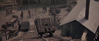 Movie still from “The Molly Maguires” (1970), directed by Martin Ritt – A train is traveling down the tracks in the middle of a city; Extreme Wide shot, High angle