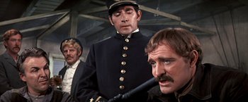 Movie still from “The Molly Maguires” (1970), directed by Martin Ritt – A man in a black uniform and a man with a gun; Medium shot, Over the shoulder angle