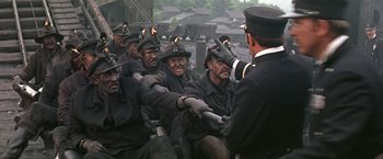 Movie still from “The Molly Maguires” (1970), directed by Martin Ritt – A group of men sitting next to each other; Medium shot, High angle