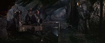 Movie still from “The Molly Maguires” (1970), directed by Martin Ritt – A man sitting on a bench in an underground area; Wide shot, High angle