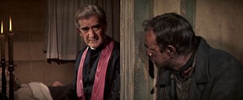 Movie still from “The Molly Maguires” (1970), directed by Martin Ritt – A man wearing a priest's collar and a pink stole; Medium shot, Over the shoulder angle