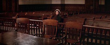 Movie still from “The Molly Maguires” (1970), directed by Martin Ritt – A woman sitting in a wooden chair in an old - fashioned courtroom; Wide shot, High angle