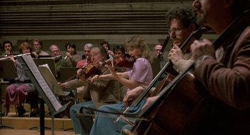 Movie still from “The Money Pit” (1986), directed by Richard Benjamin – A group of people sitting in a room playing musical instruments; Wide shot, Low angle