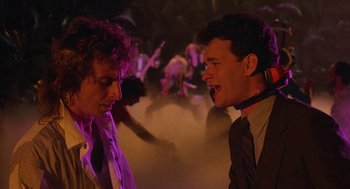 Movie still from “The Money Pit” (1986), directed by Richard Benjamin – Two men in suits talking to each other in front of a crowd of onlookers; Medium shot, Low angle