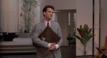 Movie still from “The Money Pit” (1986), directed by Richard Benjamin – A man in a suit and tie holding a briefcase; Medium shot, Low angle