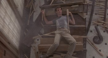Movie still from “The Money Pit” (1986), directed by Richard Benjamin – A man sitting on top of a pile of wood; Wide shot, Overhead angle