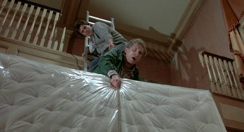 Movie still from “The Money Pit” (1986), directed by Richard Benjamin – Two men are trying to unwrap a mattress; Medium shot, Overhead angle