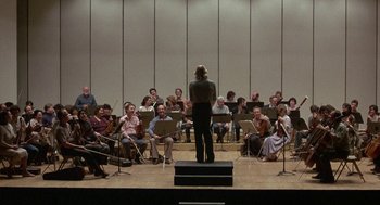 Movie still from “The Money Pit” (1986), directed by Richard Benjamin – A group of people sitting in a room with musical instruments; Extreme Wide shot, Low angle