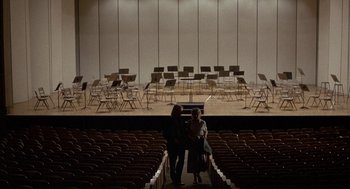 Movie still from “The Money Pit” (1986), directed by Richard Benjamin – Two people are standing in front of an orchestra; Extreme Wide shot, High angle