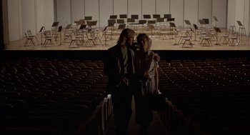 Movie still from “The Money Pit” (1986), directed by Richard Benjamin – Two people are standing in a large auditorium; Wide shot, High angle