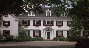 Movie still from “The Money Pit” (1986), directed by Richard Benjamin – A large white house with black shutters and a green front door; Extreme Wide shot, High angle