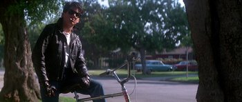 Movie still from “The Monster Squad” (1987), directed by Fred Dekker – A man in a leather jacket riding a bike; Wide shot, Low angle