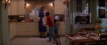 Movie still from “The Monster Squad” (1987), directed by Fred Dekker – A woman and two children in a kitchen with a television; Wide shot, Over the shoulder angle