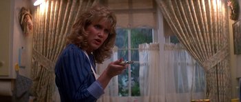 Movie still from “The Monster Squad” (1987), directed by Fred Dekker – A woman holding a cell phone in front of a window; Close Up shot, Low angle