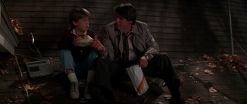 Movie still from “The Monster Squad” (1987), directed by Fred Dekker – A man sitting next to a young boy eating a sandwich; Medium shot, Low angle