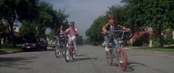 Movie still from “The Monster Squad” (1987), directed by Fred Dekker – A group of people riding bikes down a street; Wide shot, Low angle