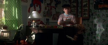Movie still from “The Monster Squad” (1987), directed by Fred Dekker – A young boy sitting at a desk in front of a lamp; Medium shot, Over the shoulder angle