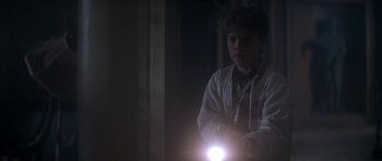 Movie still from “The Monster Squad” (1987), directed by Fred Dekker – A young boy is holding a flashlight in the dark; Medium shot, Over the shoulder angle