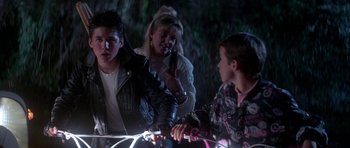 Movie still from “The Monster Squad” (1987), directed by Fred Dekker – A group of people standing next to each other near a bicycle; Medium shot, Over the shoulder angle