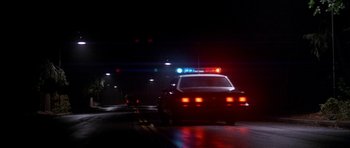 Movie still from “The Monster Squad” (1987), directed by Fred Dekker – A police car driving down a street at night; Wide shot, Low angle