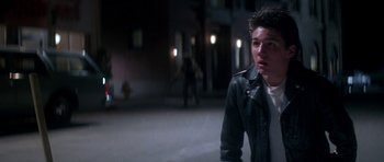 Movie still from “The Monster Squad” (1987), directed by Fred Dekker – A man in a leather jacket is sitting on the sidewalk; Medium shot, Over the shoulder angle