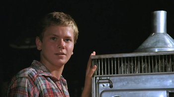 Movie still from “The Mosquito Coast” (1986), directed by Peter Weir – A young boy holding a cage in front of an oven; Close Up shot, Low angle