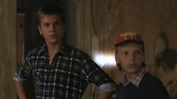 Movie still from “The Mosquito Coast” (1986), directed by Peter Weir – Two young men standing next to each other in front of a wall; Close Up shot, Low angle
