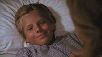 Movie still from “The Mosquito Coast” (1986), directed by Peter Weir – A young boy laying in a bed wearing headphones; Close Up shot, High angle