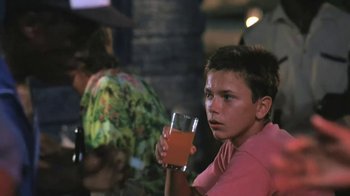 Movie still from “The Mosquito Coast” (1986), directed by Peter Weir – A young man holding a glass of orange juice in his hand; Close Up shot, Over the shoulder angle