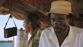 Movie still from “The Mosquito Coast” (1986), directed by Peter Weir – A man wearing a straw hat standing next to another man; Close Up shot, Over the shoulder angle
