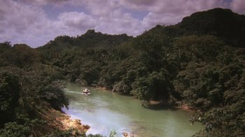 Movie still from “The Mosquito Coast” (1986), directed by Peter Weir – A boat traveling down a river surrounded by trees; Extreme Wide shot, High angle