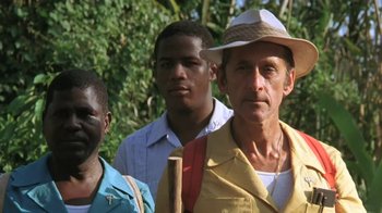 Movie still from “The Mosquito Coast” (1986), directed by Peter Weir – A group of men standing next to each other in front of trees; Medium shot, Low angle