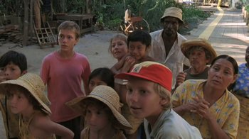 Movie still from “The Mosquito Coast” (1986), directed by Peter Weir – A group of people standing next to each other on a beach; Medium shot, High angle