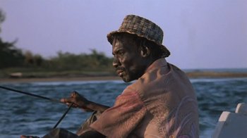 Movie still from “The Mosquito Coast” (1986), directed by Peter Weir – A man wearing a straw hat sitting on a boat; Close Up shot, Low angle