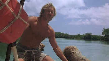 Movie still from “The Mosquito Coast” (1986), directed by Peter Weir – A shirtless man sitting on top of a boat; Medium shot, Low angle