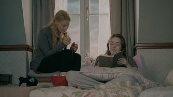 Movie still from “The Moth Diaries” (2011), directed by Mary Harron – Two women sitting on a bed and one of the women is reading a book; Medium shot, Low angle