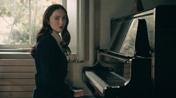 Movie still from “The Moth Diaries” (2011), directed by Mary Harron – A beautiful young lady sitting in front of a piano; Medium shot, Over the shoulder angle