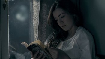 Movie still from “The Moth Diaries” (2011), directed by Mary Harron – A woman is reading a book in a dark room; Close Up shot, High angle