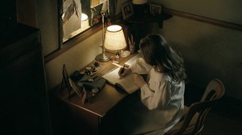 Movie still from “The Moth Diaries” (2011), directed by Mary Harron – A woman sitting at a desk writing on a notebook; Medium shot, High angle