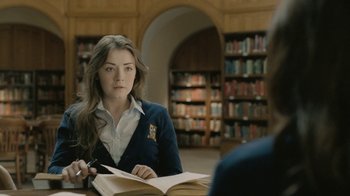Movie still from “The Moth Diaries” (2011), directed by Mary Harron – A woman sitting at a table reading a book in a library; Medium shot, Over the shoulder angle