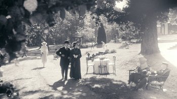 Movie still from “The Moth Diaries” (2011), directed by Mary Harron – A man and a woman standing next to each other in front of an outdoor table; Wide shot, High angle