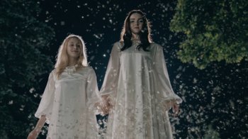 Two young women in white dresses standing next to each other in front of a tree