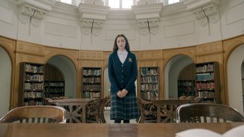 Movie still from “The Moth Diaries” (2011), directed by Mary Harron – A woman in a library standing in front of a book case; Wide shot, Low angle