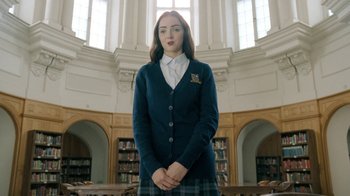 Movie still from “The Moth Diaries” (2011), directed by Mary Harron – A woman in a library wearing a blue sweater and a plaid skirt; Medium shot, Low angle